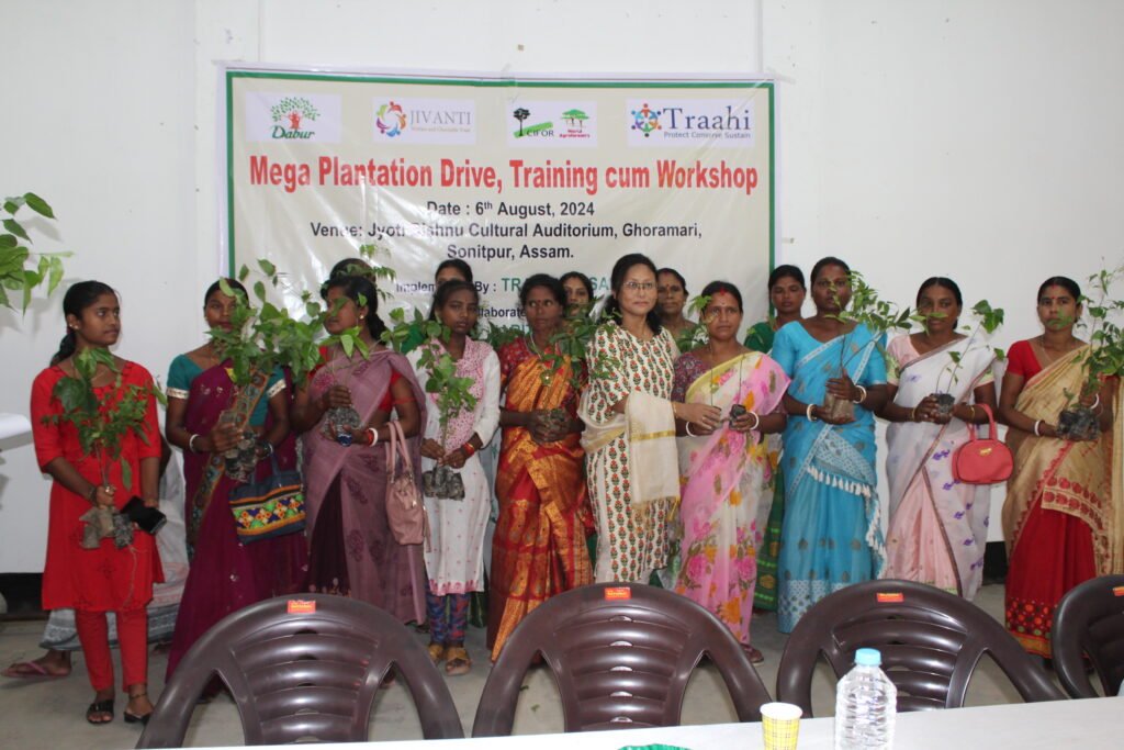 Farmers plant saplings during TRAAHI’s plantation drive in Khetri, Assam. The event, led by Kirat Biotech, symbolizes community empowerment and sustainability, with banners of supporting organizations in the background.